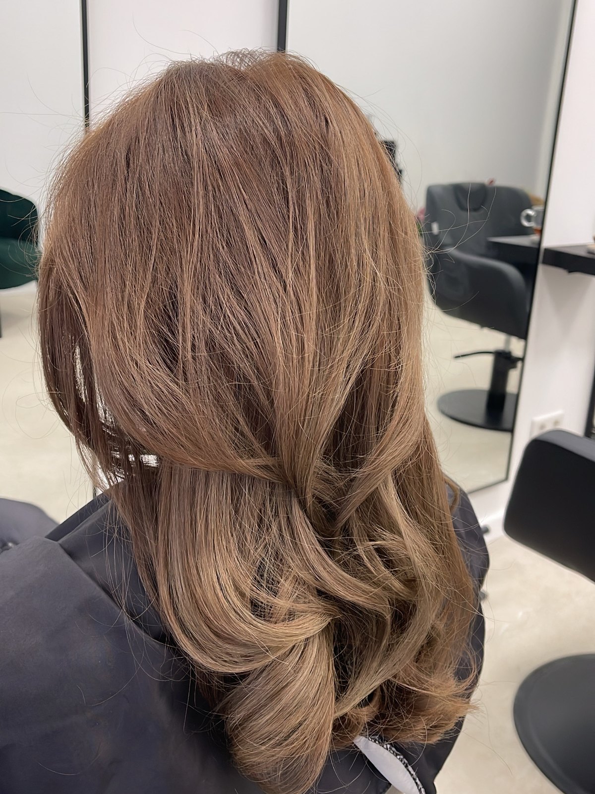Bruin haar in grote, zachte slagen geföhnd, gezien van achteren in de salon
